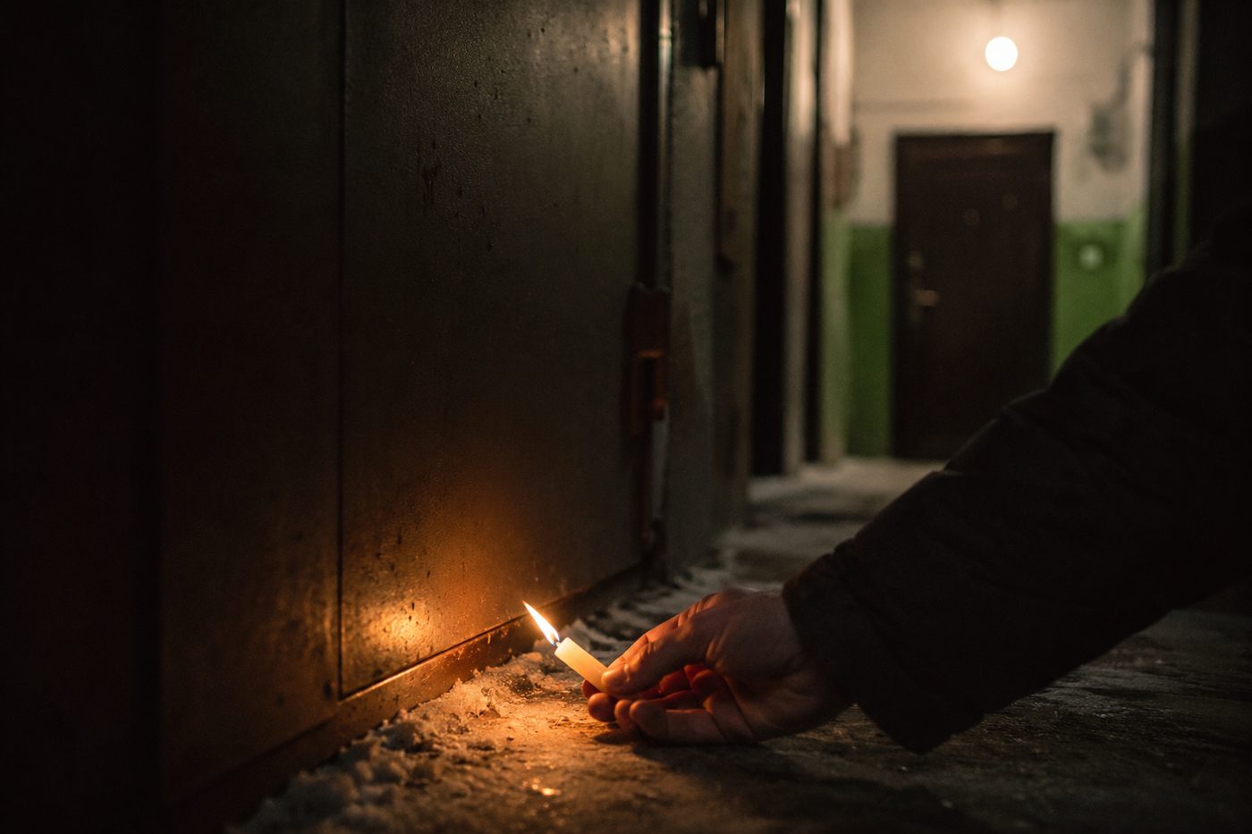 Рука со свечой у нижнего зазора входной двери, пламя отклоняется от сквозняка